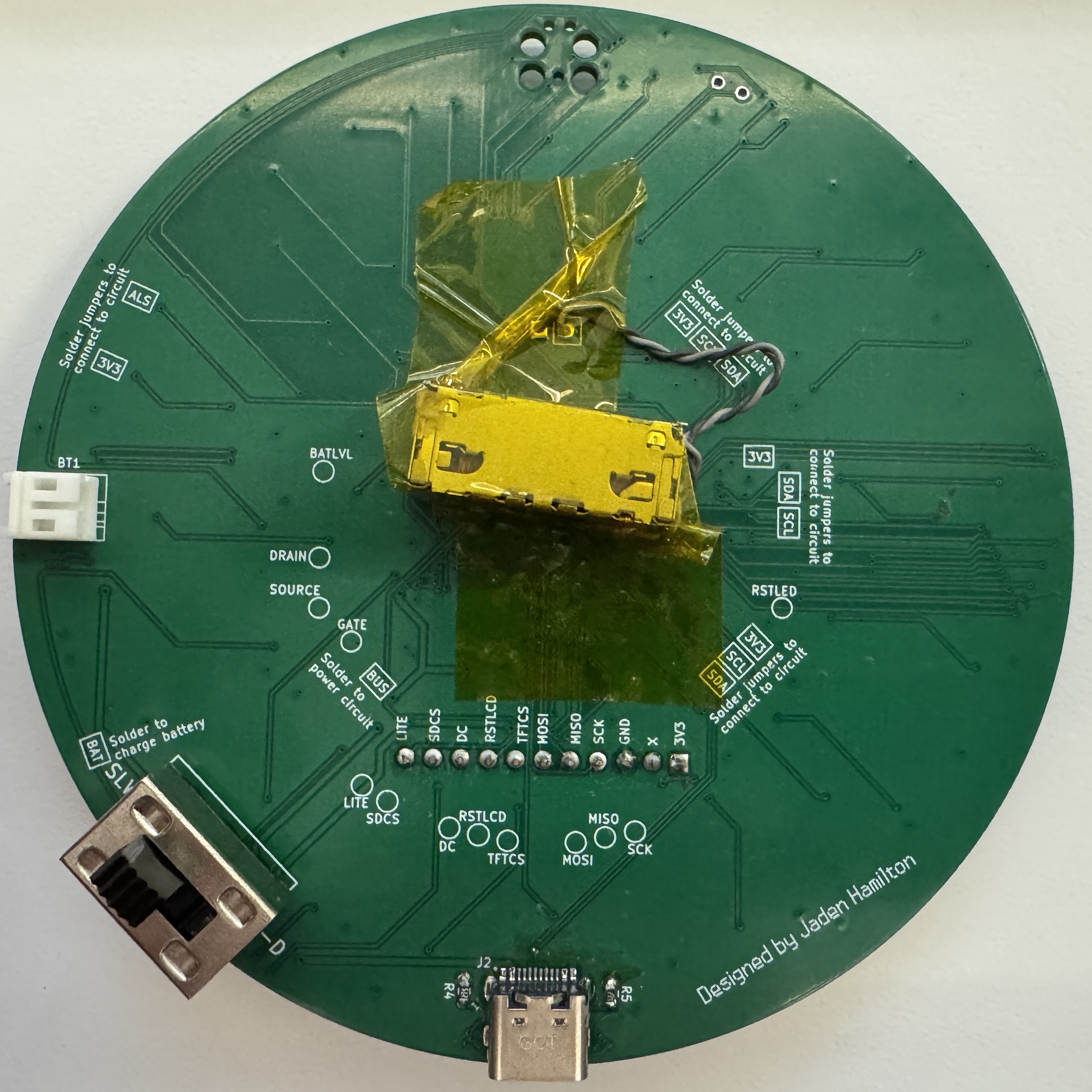 The back of a custom circuit board in the shape of a circle. An LRA motor is attached with Kapton tape.