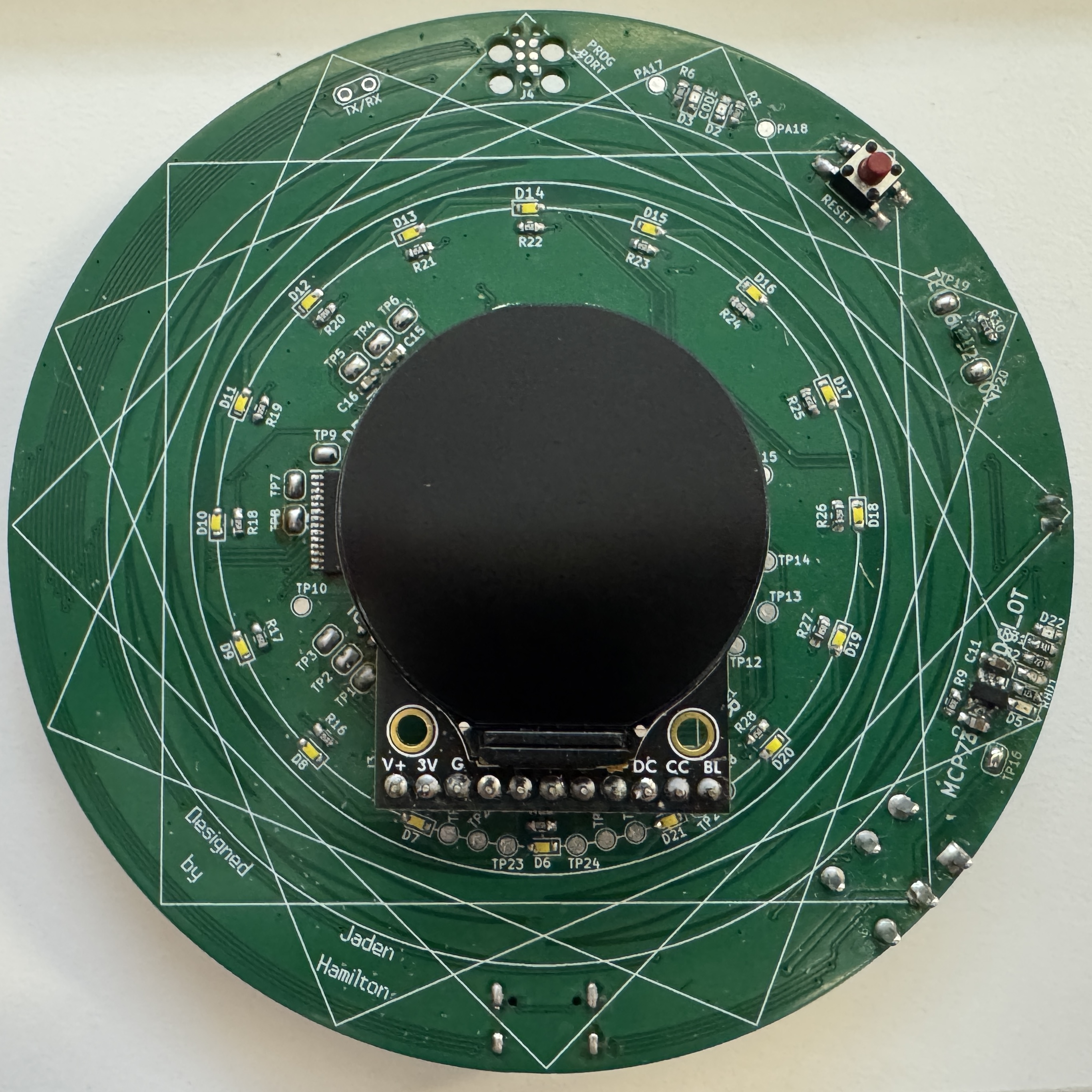 The front of a custom circuit board in the shape of a circle. It has a circular screen in the middle.